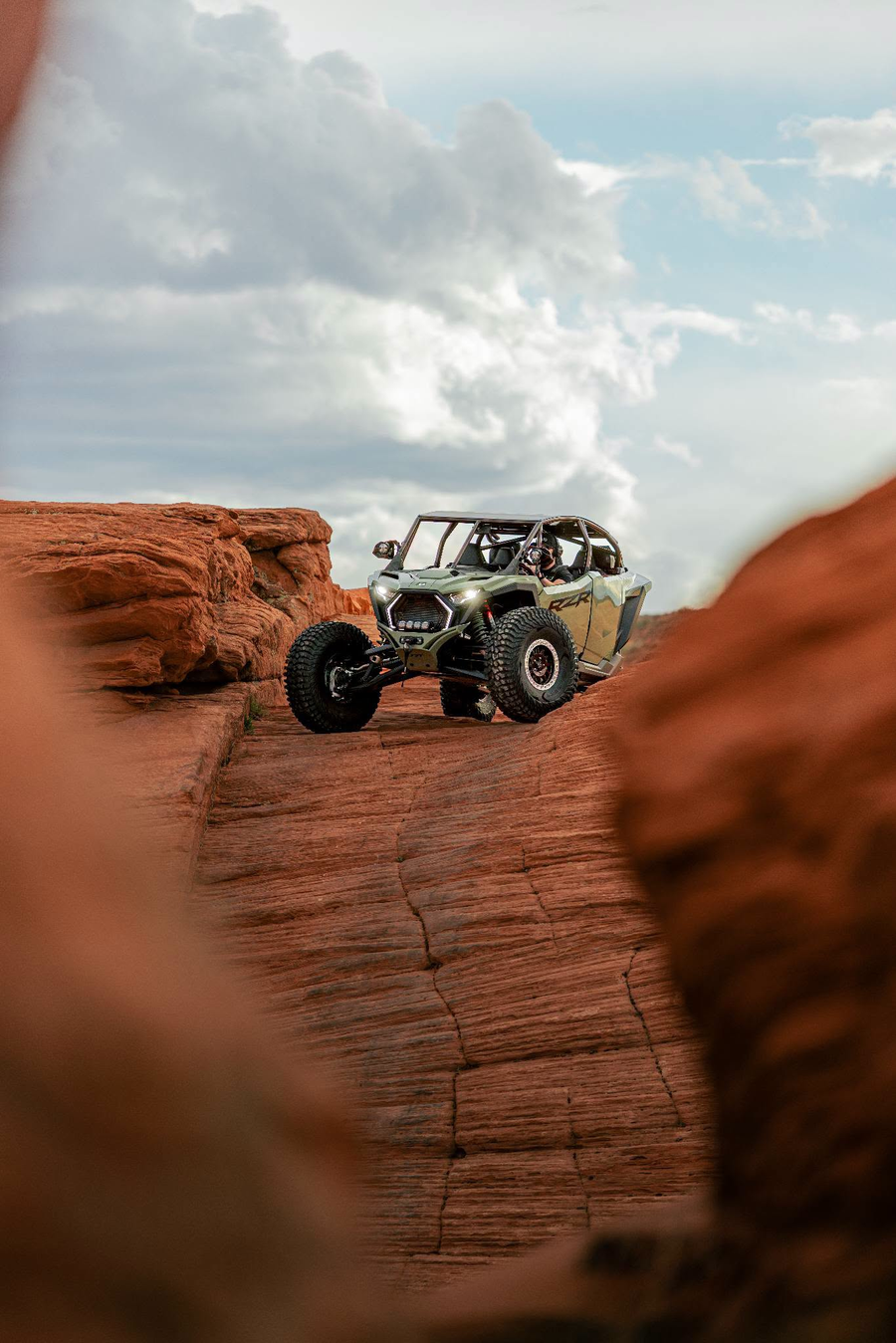 Polaris RZR with a helmeted driver navigating red sandstone terrain.